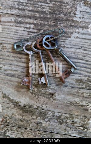 Klassische Metallschlüssel, die mit einer Sicherheitsnadel an einer Holzwand befestigt sind. Stockfoto