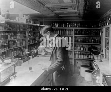 Apotheker im People's Drug Store, No. 5, 8th Street und H Street, N.E., Washington, D.C., der auf der Theke in einem mit Regalen mit Apothekenflaschen gesäumten Raum ca. zwischen 1909 und 1932 Rezepte ansah Stockfoto