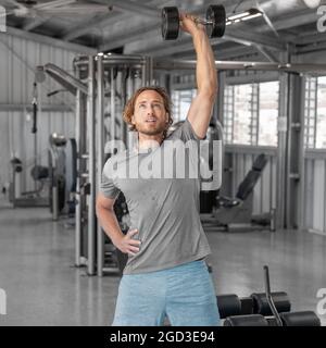 Gym Workout Fitness Mann Training mit Hanteln Heben Overhead Heben Schultern trainieren Schulterdrücken in der Halle im Health Club. Quadratisches Erntegut. Stockfoto