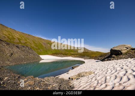 Schneefeld vom letzten Winter umgibt einen tarn im Palmer Creek Valley in Südzentralalaska. Stockfoto