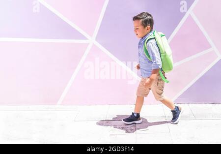 Vorschulkind, das vor einer rosa und violetten Wand zur Schule geht. Zurück zur Schule Stockfoto