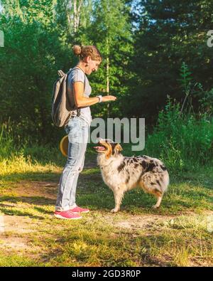 Lächelnde glückliche Frau in legerer Kleidung, die am Sommertag im Park mit Hund spielt Stockfoto