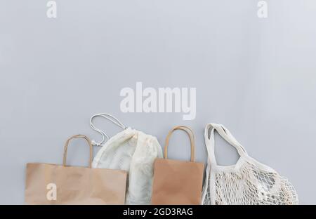 Flaches Lay mit eco white Bastelpapiertaschen und Netztaschen auf grauem Hintergrund mit Kopierfläche leerer Werbefläche. Modell der Verpackungsvorlage. Lieferung Stockfoto