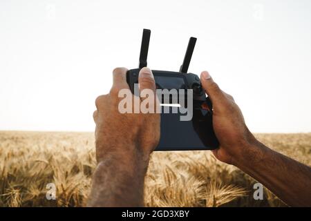 Männliche Hände mit Fernbedienung des Quadcopters im Weizenfeld Stockfoto
