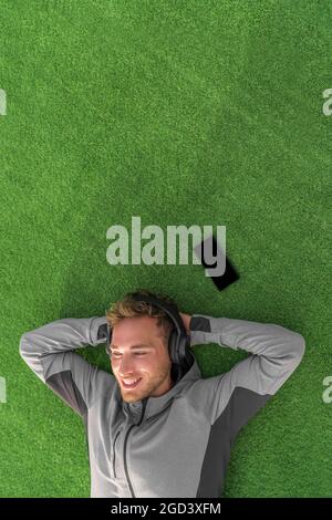 Musik hören zur Entspannung. Glücklicher Mann, der sich auf Gras legt und Podcast auf dem Mobiltelefon mit kabellosen Kopfhörern genießt. Sommerlicher Lifestyle Stockfoto