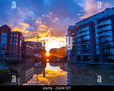 Morgensonne, die durch eine Lücke in Hafengebäuden strömt, mit einem goldenen Glanz, der sich im Wasser widerspiegelt Stockfoto