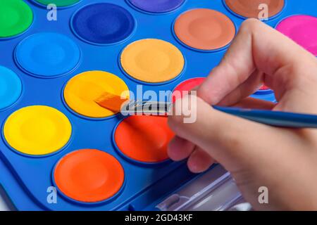 Ein Satz Aquarellfarben und ein Pinsel zum Zeichnen von Nahaufnahme. Kinderhand mit einem Pinsel. Selektiver Fokus. Stockfoto