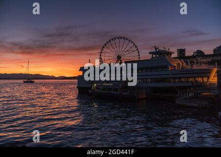 Seattle, USA. August 2021. Ein wunderschöner Sonnenuntergang über der Elliott Bay vom Pier 54 mit dem Great Seattle Wheel und Argosy Cruise Schiffen. Die Stadt hat sich bemüht, Touristen in das Tourismusviertel der Innenstadt zurückzubringen. Klimabrände und die Delta-Variante haben das Comeback des Tourismus in der Innenstadt von Seattle erheblich verlangsamt. Quelle: James Anderson/Alamy Live News Stockfoto