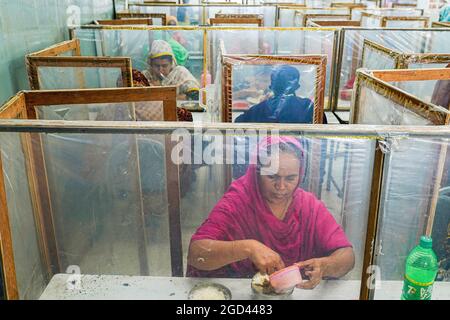 Dhaka, Bangladesch. August 2021. Arbeiter von Ready Made Garment (RMG), die durch Polythene-Barrieren getrennt sind, während sie zu Mittag essen, um die Entfernung zu wahren, als Vorsichtsmaßnahme gegen die Ausbreitung des Corona-Virus. (Foto von Sultan Mahmud Mukut/SOPA Image/Sipa USA) Quelle: SIPA USA/Alamy Live News Stockfoto