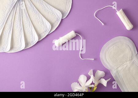 Gruppe von Produkten für den Schutz und die Menstruationshygiene mit Tampons, Wattepads, Save slip und weiße Blume auf lila Hintergrund. Draufsicht. Stockfoto