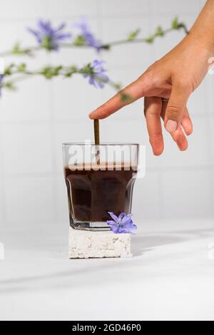 Chicorée Drink in einem transparenten Becher mit Chicorée Blumen im Vordergrund. Stockfoto