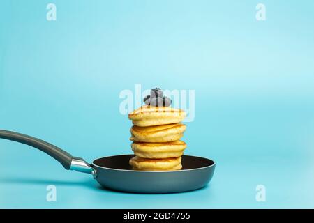 Pfannkuchen mit Beeren auf blauem Banner-Hintergrund. Üppige leckere Pfannkuchen mit Heidelbeeren und Sirup zum Brunch auf einem minimalistisch gefärbten Hintergrund. Schöne helle Lebensmittel Foto. Hochwertige Fotos Stockfoto