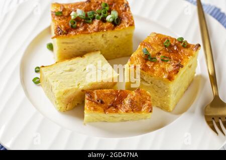 Pikante kartoffelkugel, gebackener Pudding oder Auflauf geriebener Kartoffeln auf einem weißen Teller auf einem weißen Holztisch, jüdisches Feiertagsrezept, Nahaufnahme Stockfoto