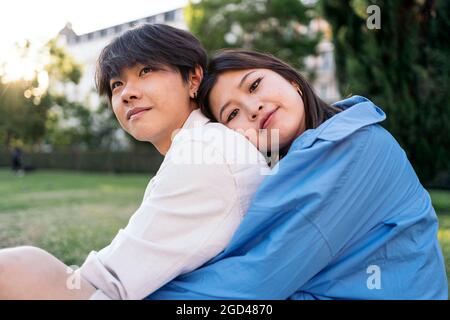 Nettes asiatisches Paar, das im Park lächelnd sitzt und die Kamera anschaut. Stockfoto