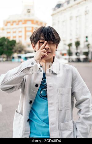 Junger und stilvoller asiatischer Mann, der das Friedenszeichen macht und die Kamera anschaut. Stockfoto