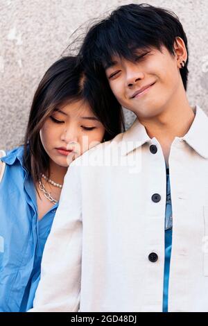 Junges asiatisches Paar, das gegen die graue Wand steht und posiert und die Kamera anschaut. Stockfoto
