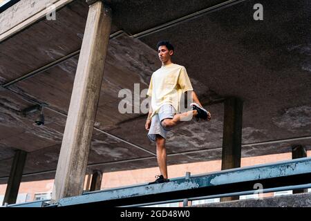 Ein junger Mann streckt sich die Beine, bevor er Parkour-Tricks in der Stadt macht. Stockfoto