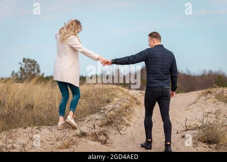 Ein junges Paar, das auf Sanddünen ging, hielt Hände.in der Ferne der Wald.Abenteuer Reise Lifestyle-Konzept. Stockfoto