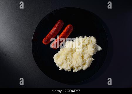 Gegrillte Würstchen mit Reis auf einem schwarzen Teller mit schwarzem Hintergrund Stockfoto