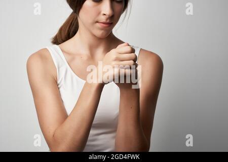 Frau in weißem T-Shirt hält Hand Gesundheitsprobleme chronische Schmerzen Stockfoto