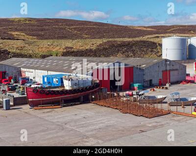 Ein kleines Fischerboot aus Holz, das am Peterson Quay neben traditionellem Lagerhaus und verschiedenen Teilen der Schiffsausrüstung gelagert wurde. Stockfoto