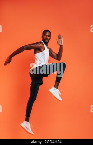 Sportler macht ein Stretching-Workout. Volle Länge der gesunden Fitness-Mann Training vor einem orangen Hintergrund. Stockfoto