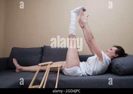 Eine Frau mit einem Cast auf ihrem Bein macht körperliche Übungen. Rehabilitation nach Verletzungen. Stockfoto