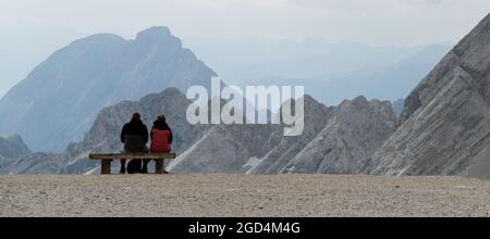 Grainau, Deutschland. August 2021. Zwei Wanderer sitzen auf einer Bank auf dem Zugspitzplatt vor einer Bergkulisse. Quelle: Angelika Warmuth/dpa/Alamy Live News Stockfoto
