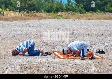 Urla, Türkei - Juni 2021: Drei muslimische Männer beten gemeinsam auf einer Kiesstraße. Islam Religion Gebet. Stockfoto