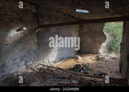 Verlassene alte Scheune in einem Dorfinneren mit Trümmern und Sonnenlicht, die durch kaputte Wand und Dach fallen Stockfoto