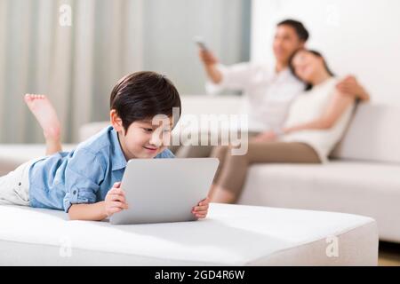 Fröhlicher Junge spielt digitales Tablet mit Eltern im Hintergrund Stockfoto