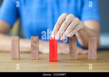 Die Frau wählt einen roten Holzblock aus vielen beigen Holzblöcken in Reihe Stockfoto