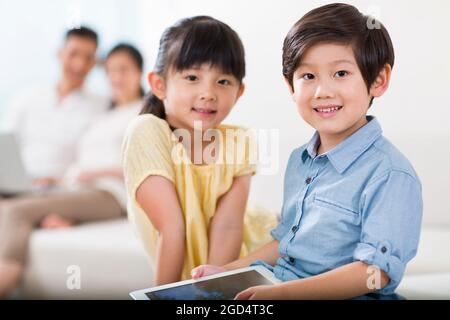 Niedliche Jungen und Mädchen mit digitalen Tablet mit Eltern im Hintergrund Stockfoto