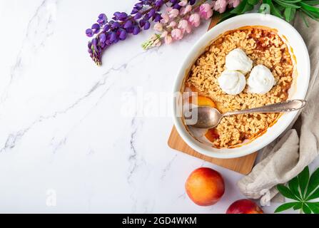 Frisch hausgemachter Nektarinkrümel mit Vanilleeis in Keramikform auf weißem Marmorboden. Draufsicht. Platz für Text. Stockfoto