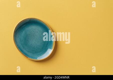 Türkisfarbene ovale Keramikplatte auf strukturiertem gelben Hintergrund. Modernes Geschirr und Geschirr in trendigen Farben für stilvolles Food-Design. Leeren Sie das Geschirr. Stockfoto