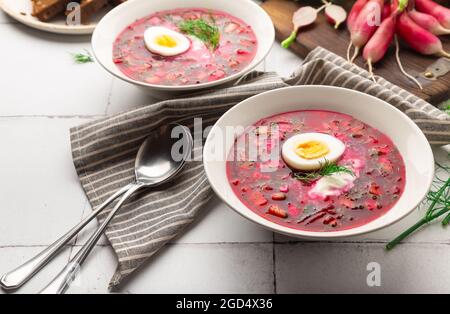 Sommerliche kalte Rote-Beete-Suppe mit saurer Rahm und Ei auf weißem Fliesengrund. Russische Küche. Selektiver Fokus. Stockfoto