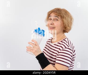 Ältere Frau trinkt Wasser, während sie auf weißem Hintergrund trainiert. Stockfoto