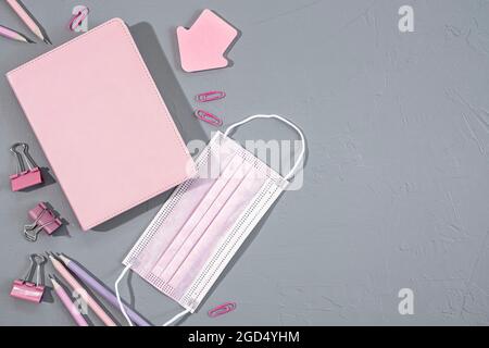 Verschiedene rosa Büro- und Schulpapiere, Bürobedarf und medizinische Maske auf grauem Hintergrund, Draufsicht Stockfoto