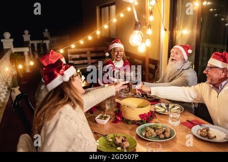 Glückliche Senioren, die beim Weihnachtsessen zu Hause mit Wein jubeln und Weihnachtsmützen tragen - konzentrieren Sie sich auf die Hände, die Gläser halten Stockfoto