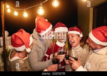 Verschiedene ältere Menschen haben Spaß Jubel mit Wein während Heiligabend tragen Weihnachtsmützen - Weiche Fokus auf Mitte Mann Gesicht Stockfoto