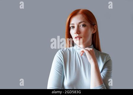 Nachdenkliche junge Frau mit langen roten Haaren und hellblauem Rollkragen Stockfoto