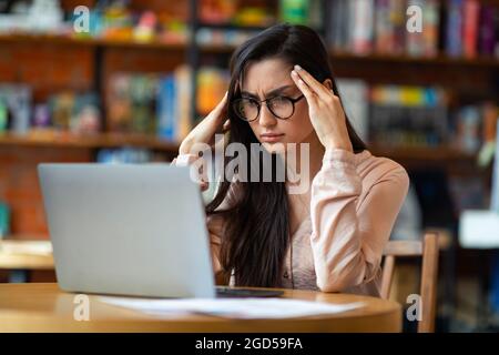 Probleme bei der Arbeit. Erschöpfte lateinische Freiberuflerin müde nach der Arbeit am Laptop, Kopfschmerzen, sitzen am Tisch im Café, Blick auf den Computer-Bildschirm A Stockfoto