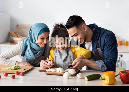 Glückliche Arabische Mutter Und Vater Lehren Ihre Kleine Tochter Wie Man Kocht, Vater Hackt Pilze Mit Niedlichen Weiblichen Kind, Liebe Islamische Familie Macht Gesundheit Stockfoto