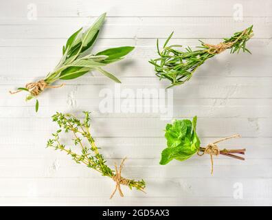 Ein Satz aromatischer Kräuter, die in kleinen Bündeln von Blumensträußen gesammelt werden. Flach lag auf weißem Holzhintergrund. Stockfoto