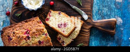 Schmale Ansicht von oben nach unten von einem Preiselbeer-Rosmarinbrot mit zwei Scheiben und Frischkäse zum Aufbreiten. Stockfoto