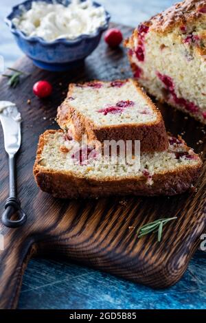 Nahaufnahme eines in Scheiben geschnittenen Cranberry Rosmarin-Schnellbrotes mit Frischkäse, der sich hinten einstreckte. Stockfoto