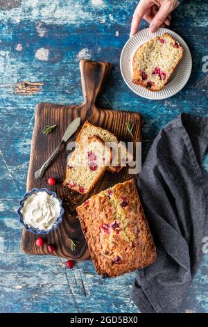 Draufsicht auf einen Cranberry-Rosmarin-Laib mit einer Hand, die einen Teller mit einer Scheibe hält, fertig zum Essen. Stockfoto