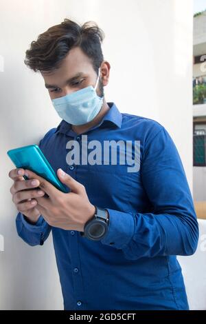 Ein junger Mann mit Gesichtsmaske und Handy Stockfoto