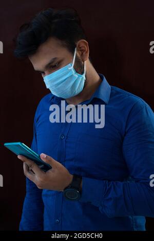 Ein junger Mann mit Gesichtsmaske und Handy Stockfoto
