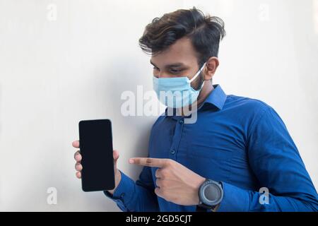 Junger, hübscher Mann zeigt auf sein Mobiltelefon in der Hand Stockfoto